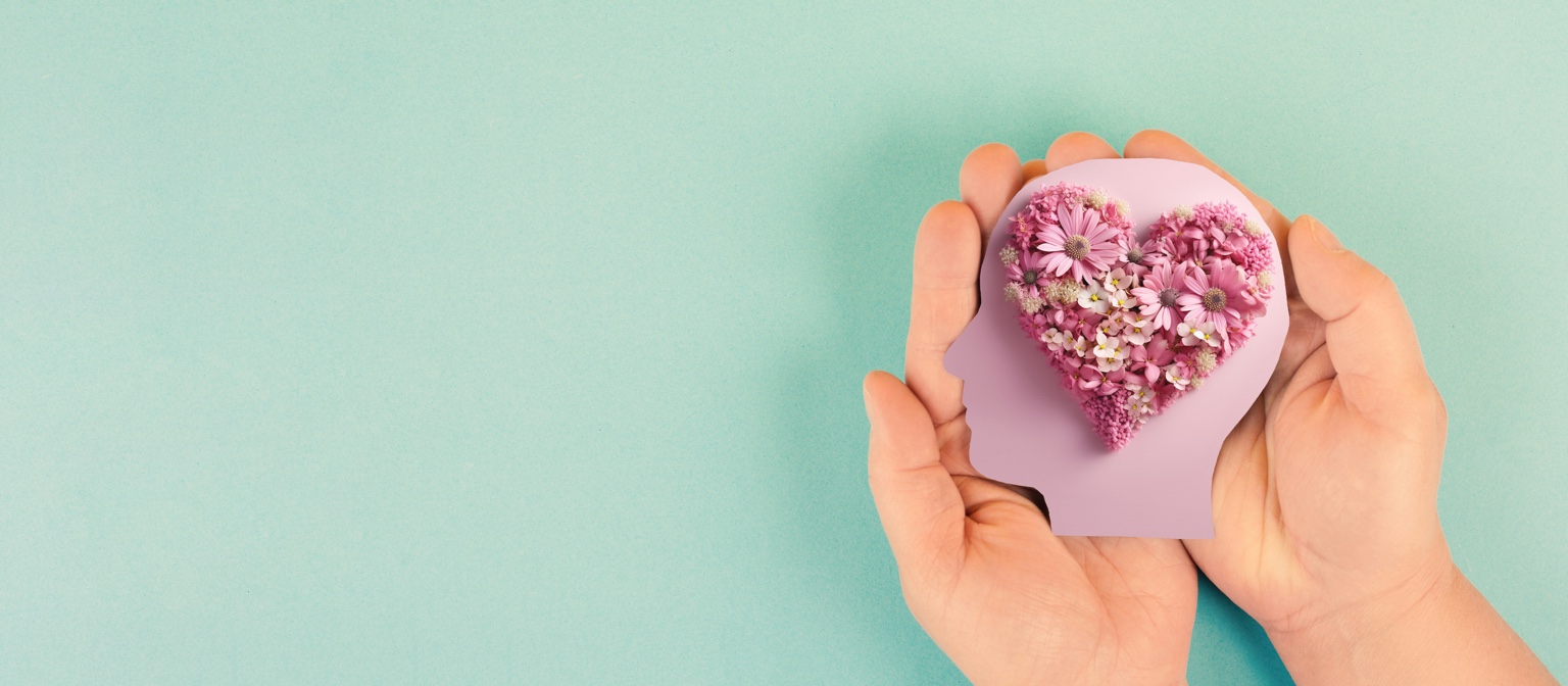 Hands holding a head-shaped card filled with flowers in a heart shape